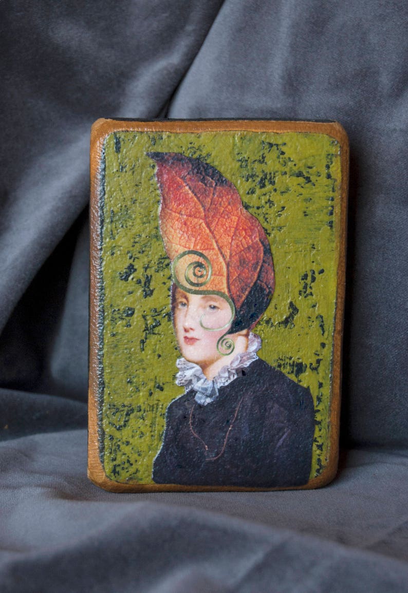 May include: A painting of a woman wearing a hat made of a large, orange and red leaf. The background is a green, textured surface.