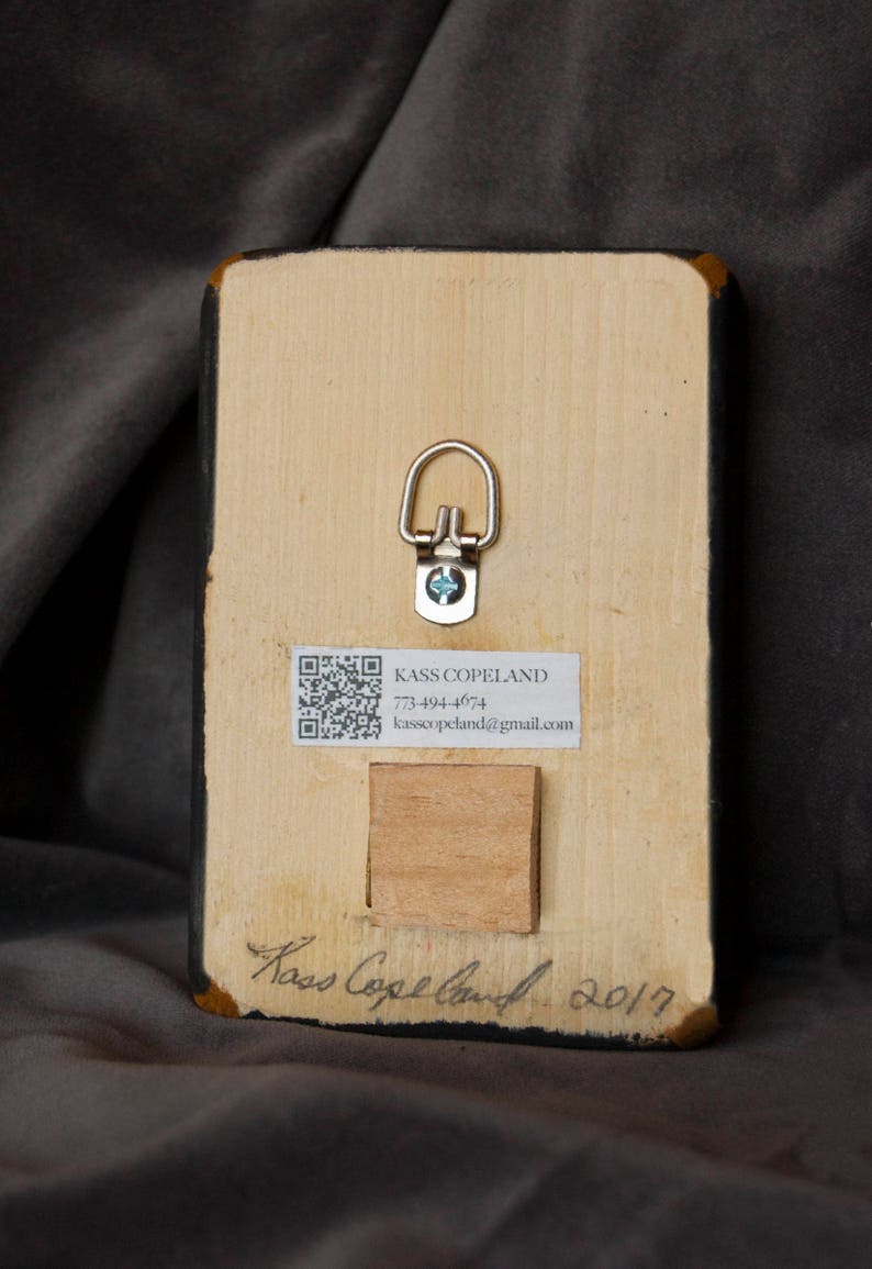May include: The back of a wooden framed painting with a QR code, contact information, and the artist's signature. The signature reads "Kass Copeland 2017".