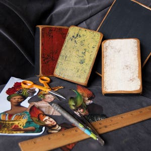 May include: Four vintage-style wooden signs with distressed paint finishes. The signs are in various colours, including red, yellow, black, and white. The signs are arranged on a dark fabric surface with a ruler, scissors, and craft paper.