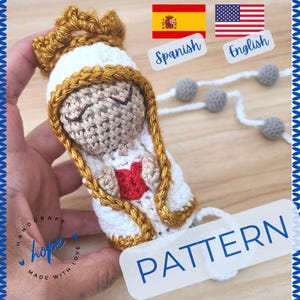 Op de afbeelding: Haakpatroon voor een witte gehaakte pop met een gouden kroon en een rood hart. De pop houdt het hart in haar handen. Het patroon is beschikbaar in zowel Spaans als Engels. De afbeelding bevat ook een kralenketting.
