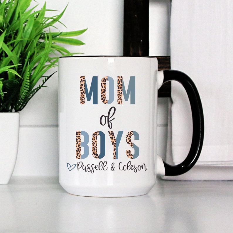 A handmade white color ceramic coffee mug with lid print name, and phrase “Mom of Boys”  is the best anniversary gift for your mother