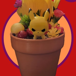 Op de afbeelding: Een terracotta bloempot met een geel Pikachu-figuurtje, gele en roze bloemen en rode bessen.
