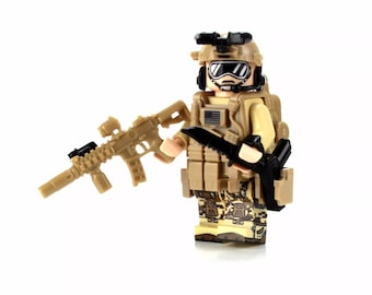 May include: A tan and black military action figure with a black helmet, goggles, and a tan vest. The figure is holding a tan and black rifle and a black knife.