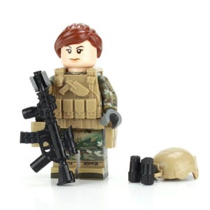 May include: A female Lego minifigure wearing a camouflage uniform and a tactical vest, holding a black rifle. She has brown hair and is wearing a black helmet.