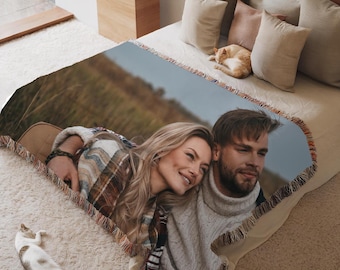 May include: A woven throw blanket with a photo of a couple embracing in a field. The couple is wearing casual clothing and smiling at each other.