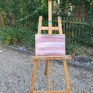 May include: A wooden easel with a pink and white abstract painting on canvas.