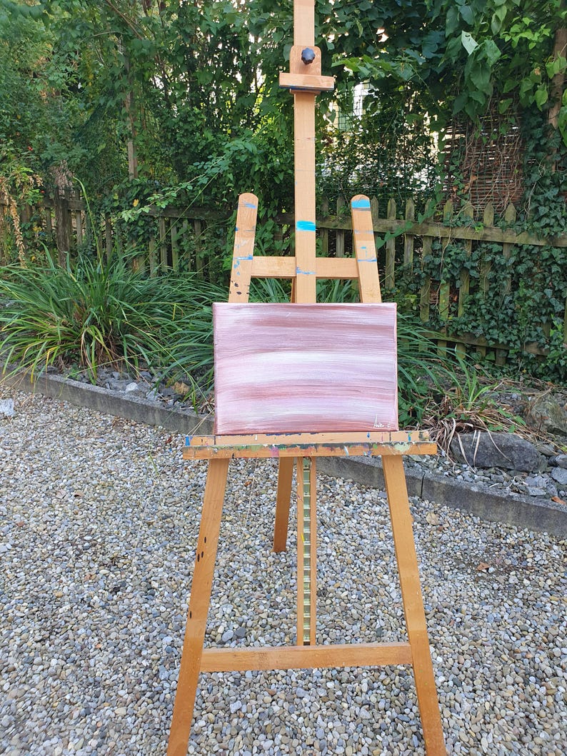 May include: A wooden easel with a pink and white abstract painting on canvas.