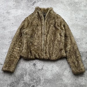 Könnte beinhalten: Eine braune Kunstfelljacke mit Reißverschluss. Die Jacke hat einen hohen Kragen und lange Ärmel.