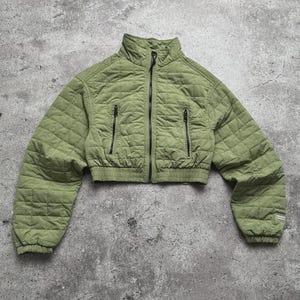 Peut inclure: Veste courte matelassée vert olive avec col montant et fermetures éclair noires. La veste présente un motif en losanges et deux poches avant. Les manches sont longues et l'ourlet inférieur est élastiqué.