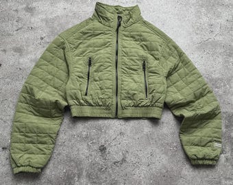May include: A cropped, olive green quilted jacket with a high collar and black zippers. The jacket features a diamond pattern and two front pockets. The sleeves are long and the bottom hem is elasticized.