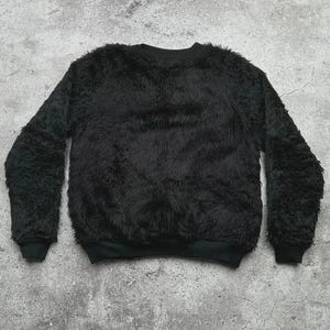 Op de afbeelding: Een zwarte, donzige sweatshirt met een ronde hals en lange mouwen. De sweatshirt heeft een zacht, getextureerd uiterlijk en de manchetten en zoom zijn effen zwart.