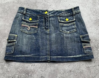 Puede incluir: Una minifalda vaquera azul con botones amarillos y bolsillos. La falda tiene un aspecto desgastado y está hecha de una tela suave y cómoda.