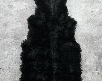 May include: A black faux fur vest with a hood. The vest is sleeveless and has a soft, plush texture. The hood is attached and adds warmth and style. The vest is designed to be worn as an outer layer.
