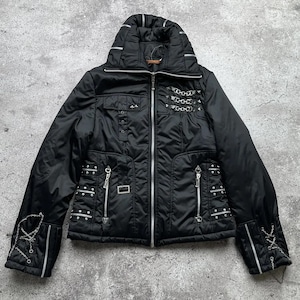 Könnte beinhalten: Schwarze Steppjacke mit silberner Hardware, darunter Ketten, Nieten und Reißverschlüsse. Die Jacke hat einen hohen Kragen und einen Reißverschluss.