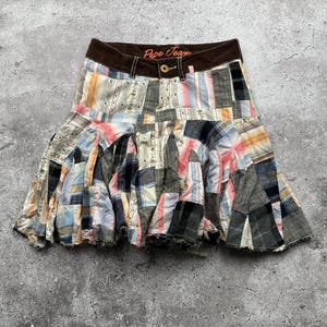 Puede incluir: Una falda de patchwork con una cintura marrón y el texto "Pepe Jeans" en naranja. La falda está hecha de diferentes telas y patrones, incluyendo cuadros, rayas e estampados florales.