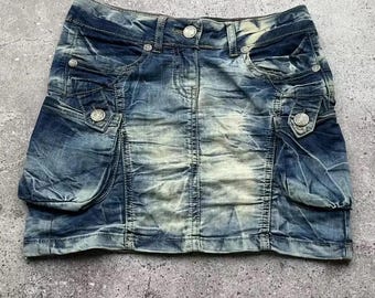 Puede incluir: Una minifalda vaquera azul con detalles desgastados y bolsillos grandes. La falda tiene un aspecto descolorido y está hecha de una tela suave y cómoda.