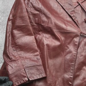 May include: A burgundy leather blazer with a notched lapel and long sleeves. The blazer has a classic design with a tailored fit, and a red lining is visible. The leather appears to be slightly distressed, adding to its vintage appeal.