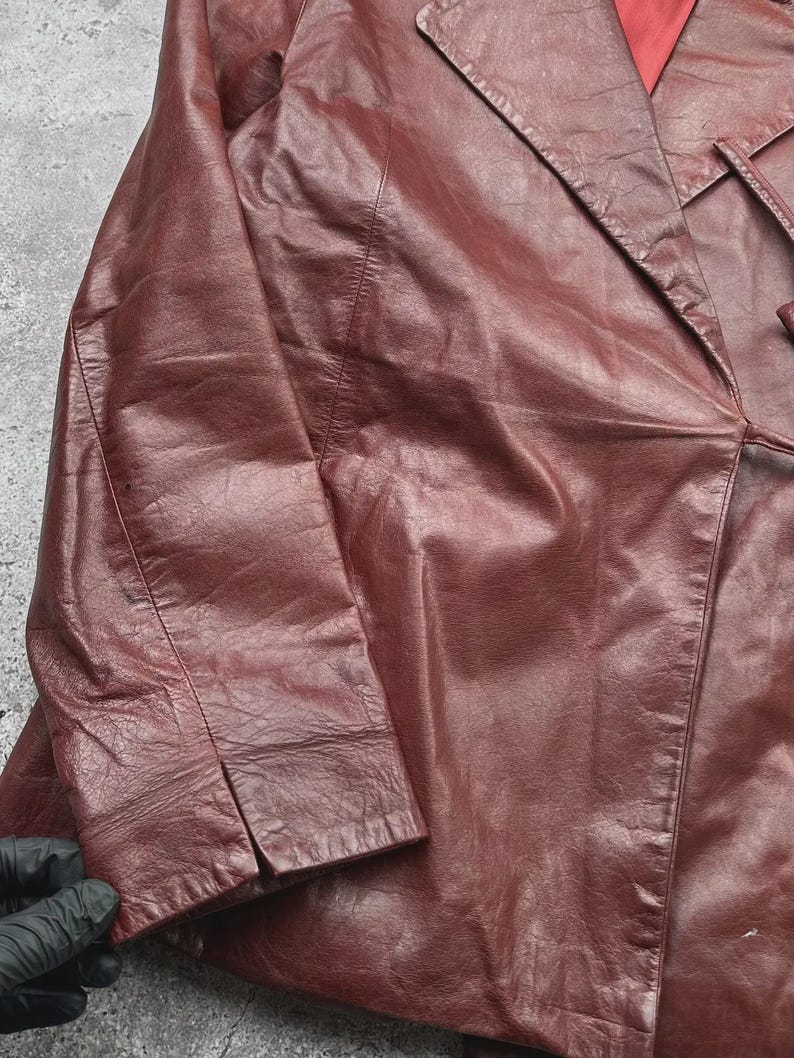 May include: A burgundy leather blazer with a notched lapel and long sleeves. The blazer has a classic design with a tailored fit, and a red lining is visible. The leather appears to be slightly distressed, adding to its vintage appeal.