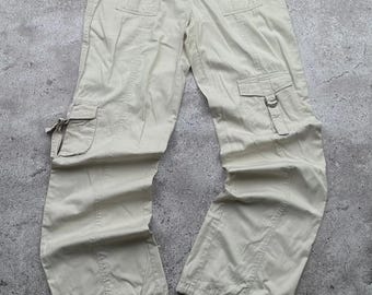 Könnte beinhalten: Beige Cargohose mit mehreren Taschen und Kordelzügen an den Knöcheln. Die Hose hat einen Knopf- und Reißverschluss und ist aus einem leichten Stoff gefertigt. Die Hose liegt flach auf einer grauen Oberfläche.