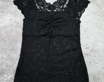 Può includere: Top in pizzo nero con scollo rotondo e maniche corte. Il top è realizzato in un tessuto di pizzo delicato e ha un aspetto leggermente drappeggiato sul seno.