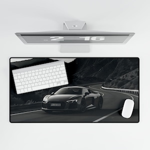 May include: Black and white desk mat featuring a black sports car driving on a winding road. A white keyboard and a white mouse are also included in the image.