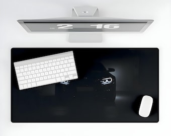 May include: Black desk mat with a dark silhouette of a car with headlights on. The mat has a white keyboard and a white mouse on it.