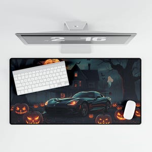 May include: A black desk mat featuring a Halloween scene with a sports car, jack-o'-lanterns, a haunted house, and a ghost. A white keyboard and mouse are on the mat. A computer monitor is above the mat.