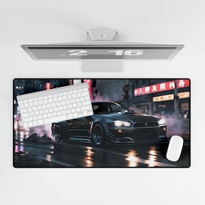 Pode incluir: Um carro preto com um teclado branco e um rato branco sobre um tapete de rato preto e cinzento com uma cena de rua da cidade no fundo. O carro é um carro desportivo japonês com um grande spoiler e uma carroçaria larga. A cena da rua acontece à noite e os edifícios são iluminados com letreiros de néon. O tapete de rato é feito de um material macio e durável e é projetado para fornecer uma superfície lisa para jogos ou uso diário.
