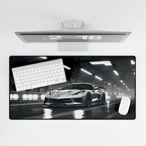 May include: A black and white mousepad with a white sports car on a dark road. The car is in focus and the road is blurred. The mousepad is rectangular and has a smooth surface.