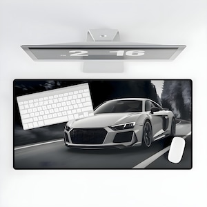 May include: A black and white mousepad with a white keyboard and a white sports car on a black asphalt road. The car is driving towards the right side of the image.