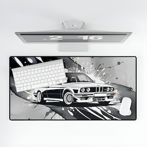 May include: A black and white mousepad with a black and white image of a car and paint splatters. The car is a white BMW with black accents. A white keyboard is on the left side of the mousepad.