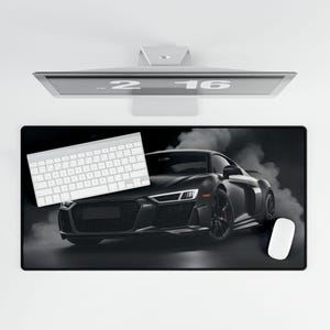 May include: Black and white desk mat with a black sports car and smoke coming from the exhaust. A white keyboard and a white mouse are on the mat.