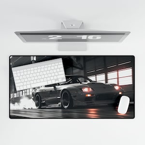 May include: A black and white photograph of a silver sports car driving on a race track. The car has red tail lights and a black spoiler. The car is in motion and there is a trail of smoke behind it.