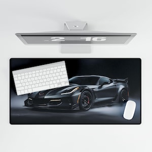 May include: A black and gray car mousepad with a black sports car on a dark background. The car has a black interior and a white keyboard is on top of the mousepad.