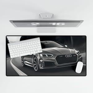 May include: Black and white photo of a black Audi S5 car driving on a road. The car is in focus and the background is blurred. The car has a black grille with the Audi logo and a black spoiler.