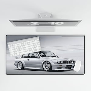 May include: A white desk mat with a gray and white keyboard and a white mouse. The mat features a gray illustration of a silver BMW E30.