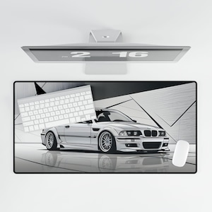 May include: A white BMW with black accents on a black and white geometric design mousepad. The mousepad is on a white surface. A white keyboard is on the left side of the mousepad. A white computer monitor is in the background.