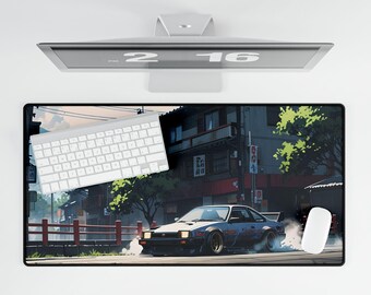 May include: A rectangular desk mat featuring a Japanese street scene with a drifting sports car. The mat has a black border and a white keyboard and mouse are on top. The monitor above displays the time 2:16.