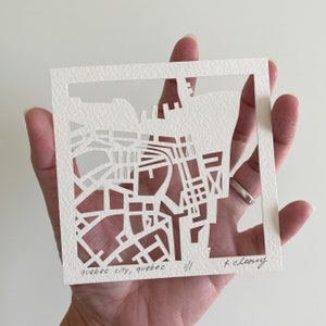 May include: A white paper cutout of a map of Quebec City, Canada. The map is framed with a white border and the text "quebec city, quebec //" is written at the bottom left corner. The artist's signature "K. OLeary" is written at the bottom right corner.