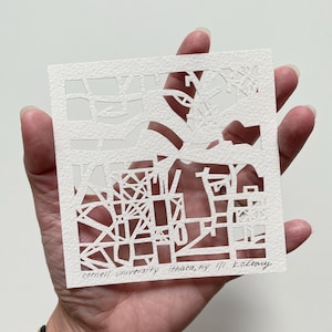 May include: A white paper cut-out art piece depicting a map of Cornell University in Ithaca, NY. The artist's signature, "K. O'Leary", is visible in the bottom right corner.
