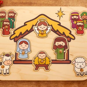Könnte beinhalten: Holzpuzzle mit Krippenszene mit Stall, Engel, Stern und Figuren wie Maria, Josef, Jesuskind und den Heiligen Drei Königen. Enthält eine Kuh und ein Schaf. Die Puzzleteile sind farbenfroh und cartoonartig.
