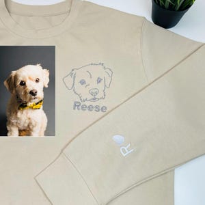 May include: A beige sweatshirt with a photo of a dog and the name "Reese" embroidered on the front. The dog's name is also embroidered on the sleeve with a paw print.
