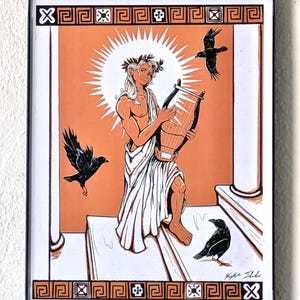 May include: Framed art print featuring a classical illustration of a figure playing a lyre, surrounded by crows. The artwork has an orange background with white and black accents, and a decorative border. The figure is wearing a laurel wreath and draped in white cloth.