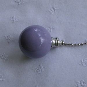 May include: A smooth, spherical light purple ceiling fan pull chain ornament with a glossy finish. The round lavender knob is attached to a polished silver-toned metal connector and a standard silver-colored beaded metal pull chain extension.