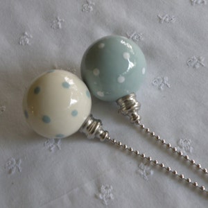 May include: Two decorative bottle stoppers with spherical tops. One is off-white with light blue polka dots, the other is light blue with white polka dots. Both have silver-colored metal bases and ball chains.