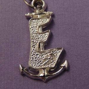 May include: Silver charm with the letter E and an anchor. The letter E is stylized and has a textured surface.