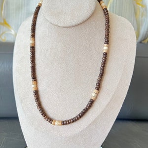 May include: A brown and beige wooden bead necklace on a white mannequin.
