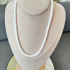 May include: A white shell necklace displayed on a mannequin. The necklace is made from small, round shells that are strung together.