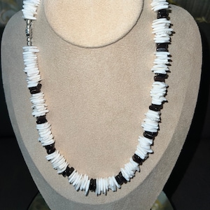 May include: A white and black shell necklace with a silver clasp. The necklace is made of flat, rectangular shell pieces.