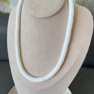 May include: A white shell necklace made of small, round, flat shells. The necklace is displayed on a white mannequin bust.